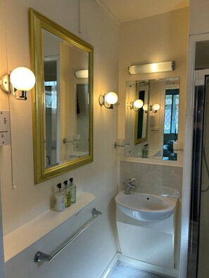 A bathroom with a large mirror, a sink, and wall-mounted lights. - Oakwood Bed and Breakfast Heathrow (West Drayton)