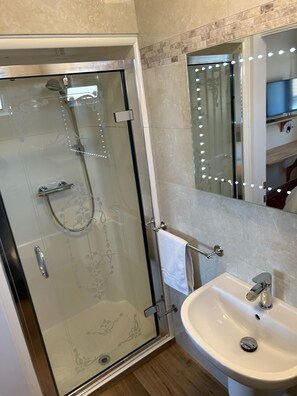 A bathroom with a glass-enclosed shower, a white sink, and a mirror with lights. - Oakwood Bed and Breakfast Heathrow (West Drayton)