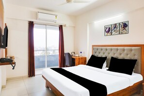 Habitación de hotel con cama, escritorio, silla, teléfono, unidad de aire acondicionado, ventana con cortinas y una obra de arte en la pared.