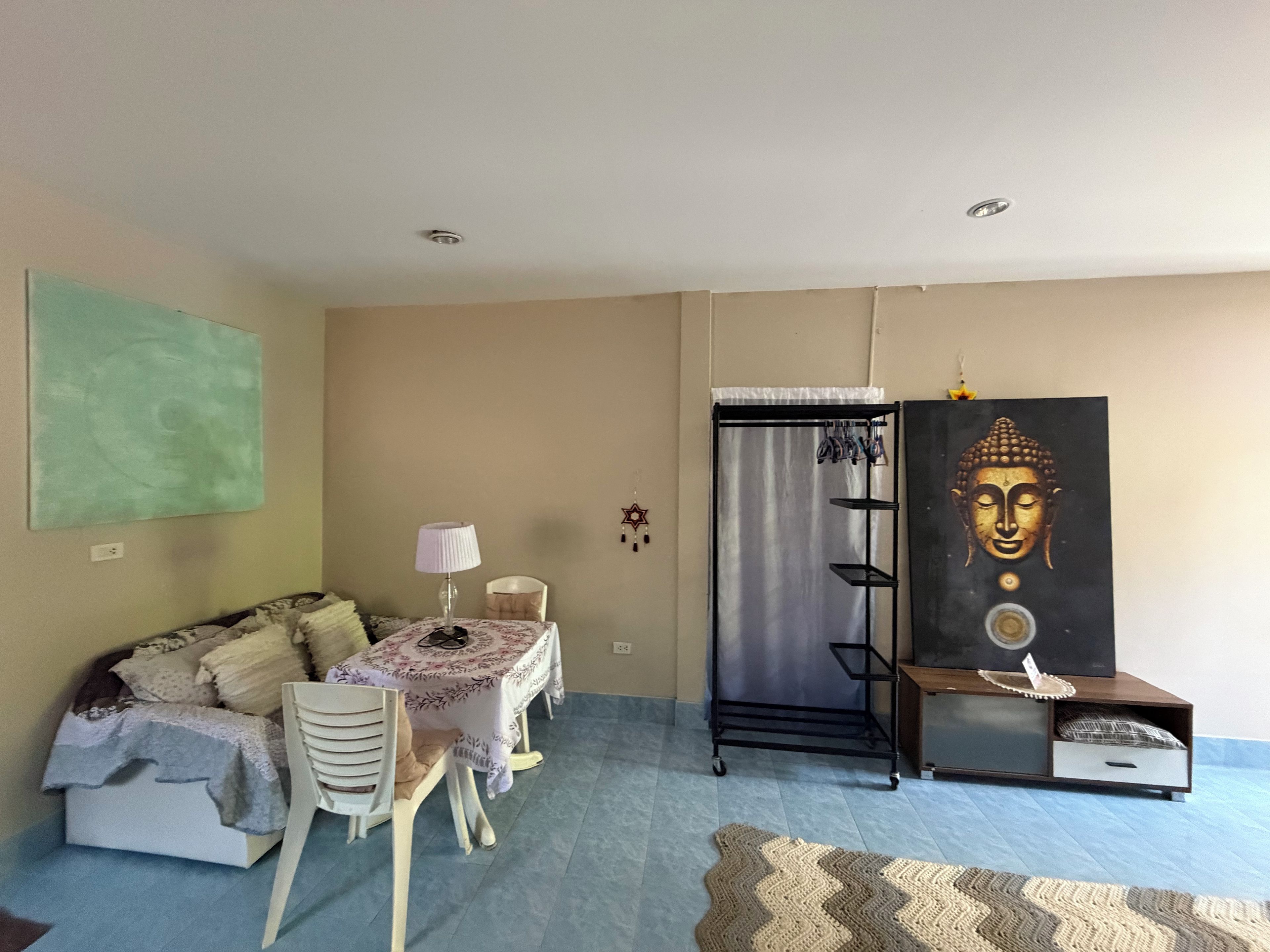 Une chambre avec un lit, une table avec une lampe, une armoire et un tableau représentant un Bouddha.