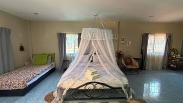 Une chambre avec un lit à baldaquin, un canapé-lit, un bureau avec une chaise et un ventilateur.