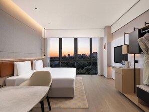 Una habitació d'hotel moderna amb un llit, escriptori, cadira, televisió i vista a la ciutat.