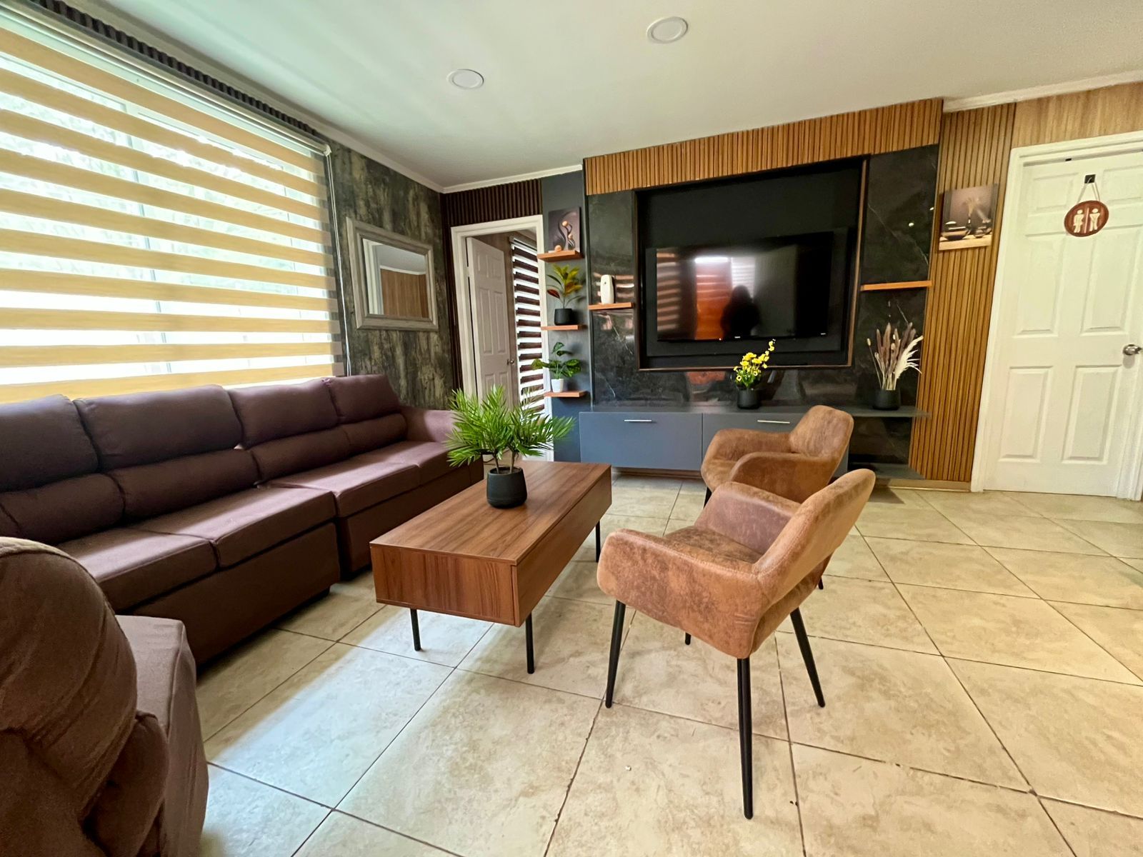 Una sala de estar moderna con un sofá marrón, una mesa de centro de madera y dos sillones.