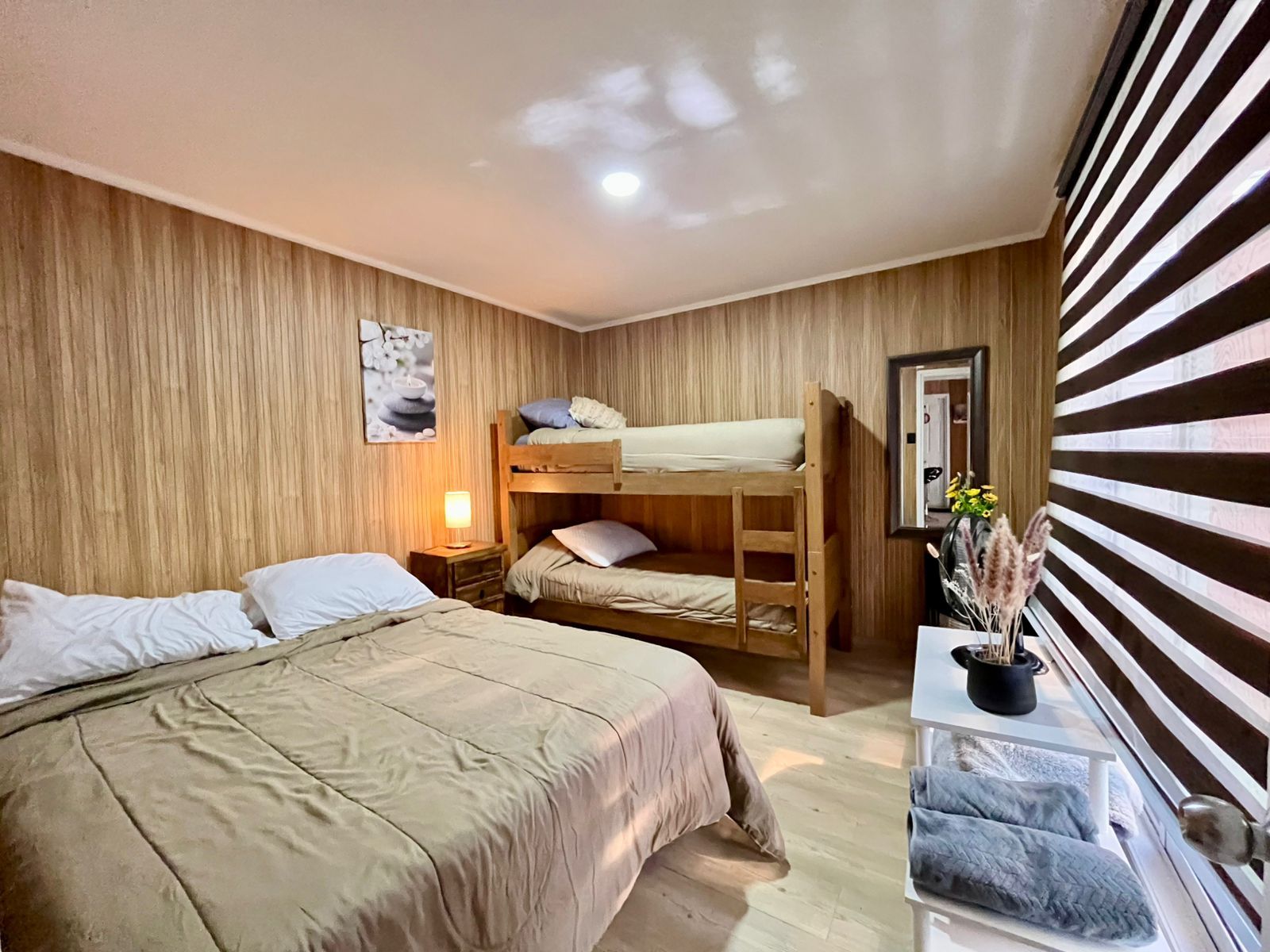 A room with a bunk bed, a bedside table with a lamp, a mirror, and a wall-mounted shelf with decorative items.