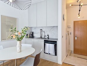 Una cocina moderna con armarios blancos, un lavamanos de acero inoxidable y una zona de comedor con mesa y sillas blancas.