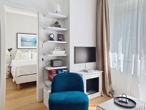 Ein Hotelzimmer mit Bett, Schreibtisch mit Computer, Fernseher, Bücherregal und Fenster mit Vorhängen.