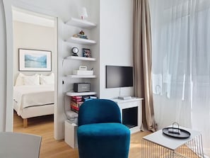 Ein modernes Hotelzimmer mit einem Bett, einem Schreibtisch mit Computer, einem blauen Stuhl und einem Fernseher.