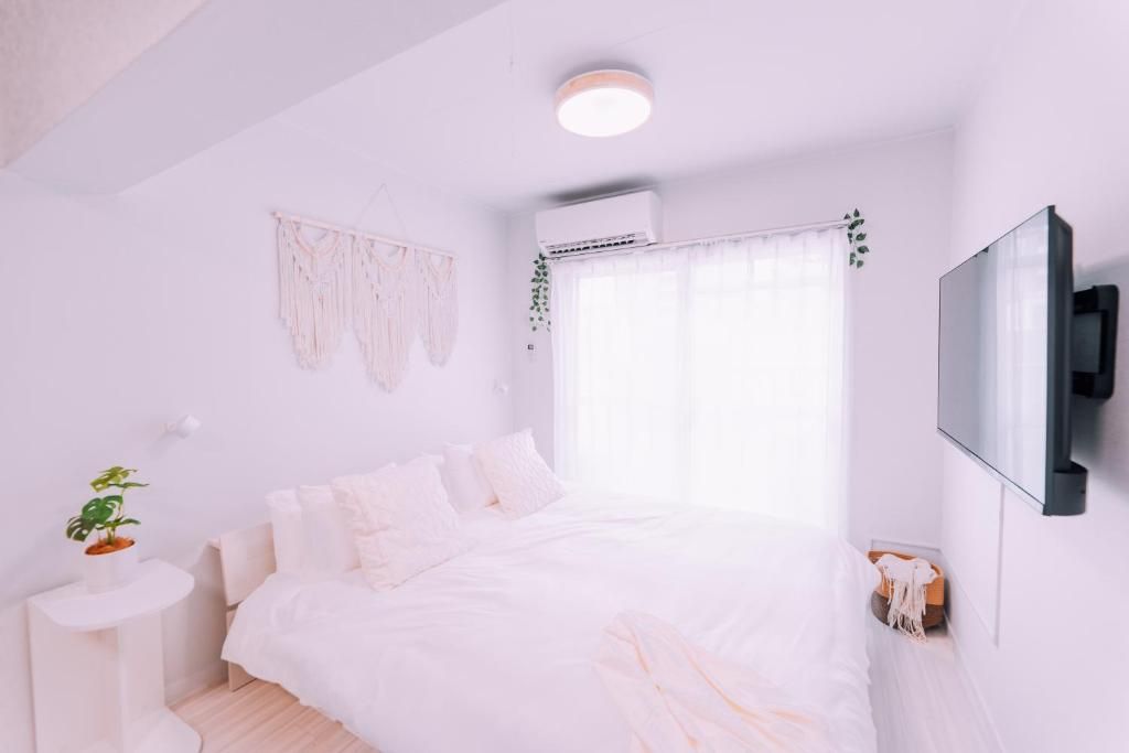 A bedroom with a bed, a bedside table with a plant, a wall-mounted TV, and a window with curtains.