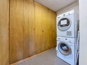 Een wasruimte met een gestapelde wasmachine en droger, een houten garderobe en een betegelde vloer.