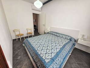Ein Schlafzimmer mit einem großen Bett, zwei Stühlen, einem Nachttisch und einer Tür zu einem weiteren Raum.