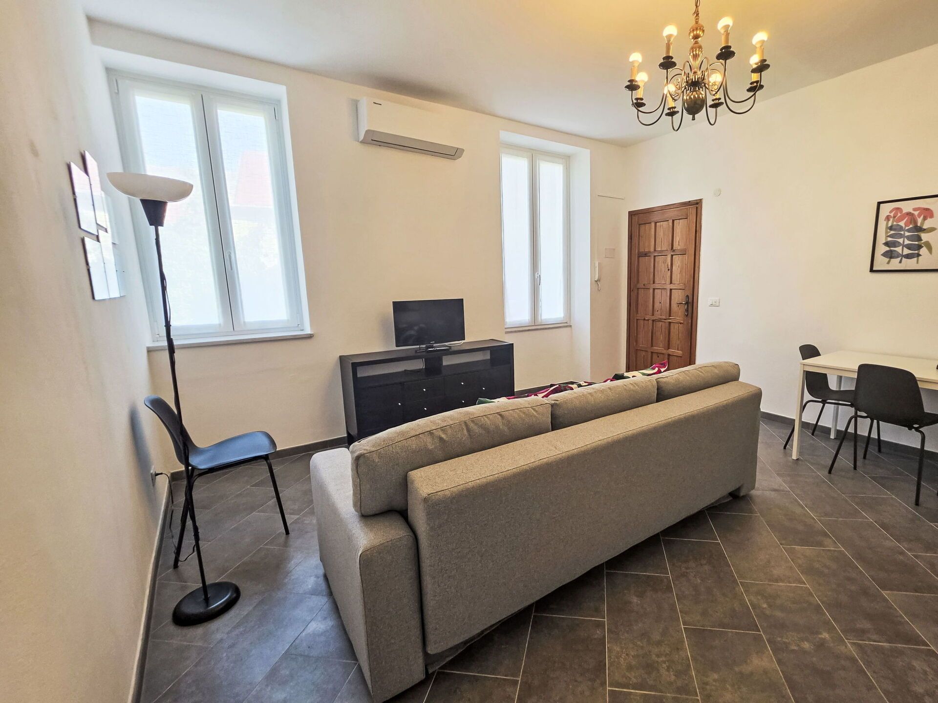 A living room with a sofa, a television, a dining table with chairs, and a chandelier.