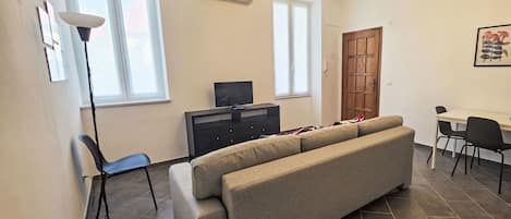Ein Wohnzimmer mit einer Couch, einem Fernseher, einem Esstisch mit Stühlen und einer Kristallleuchter.