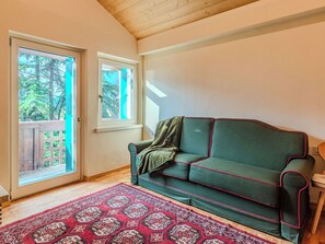 Una habitación acogedora con un sofá verde, una alfombra estampada y un techo de madera.