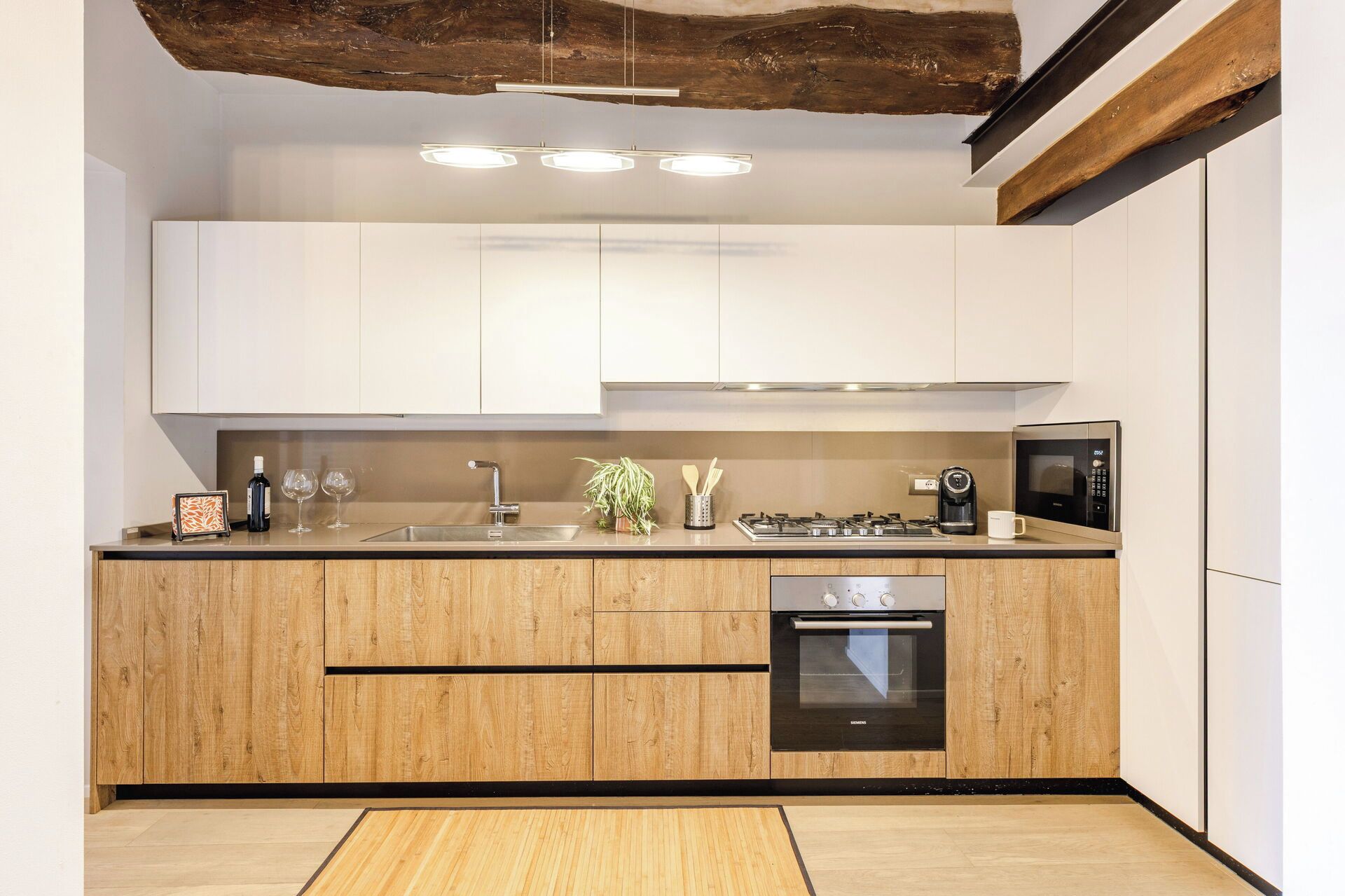 Une cuisine moderne dotée de meubles en bois, d’un évier en acier inoxydable, d’un four encastré et d’un four à micro-ondes.