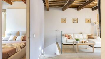 A modern living room with a white sofa, a glass coffee table, and a wooden ceiling.