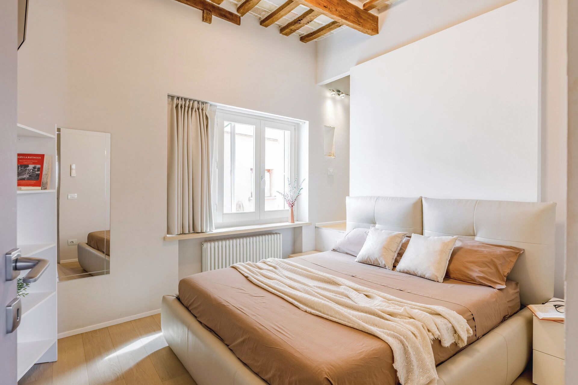 Ein Schlafzimmer mit Bett, Fenster mit Vorhängen, Heizkörper und Nachttisch.