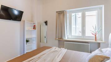 Een slaapkamer met een bed, een witte kledingkast, een radiator, een raam met gordijnen en een plant op de vensterbank.