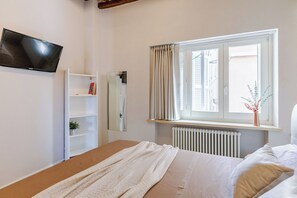 Un dormitori amb un llit, un armari blanc, un radiador, una finestra amb cortines i una planta al davant de la finestra.