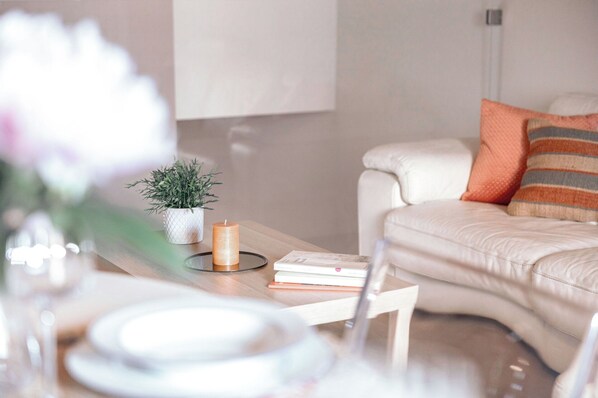 Ein modernes Wohnzimmer mit einem weißen Sofa, einem kleinen Tisch mit Kerze, einer Topfpflanze und einem Buch.