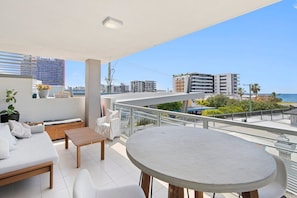 A balcony with a sofa, a table, and a view of the sea and buildings. - Sea and Salt - Palm Beach Coastal Escape (Gold Coast)