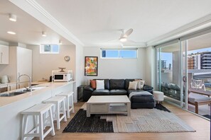 A modern living space with a kitchen, a sofa set, and a dining area. - Sea and Salt - Palm Beach Coastal Escape (Gold Coast)