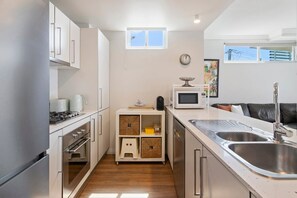 A compact kitchen with stainless steel appliances, a microwave, and a sink. - Sea and Salt - Palm Beach Coastal Escape (Gold Coast)