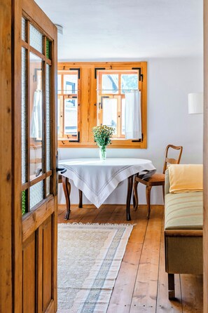 Ein Zimmer mit einem Holztisch, Stühlen, einem Fenster mit Vorhängen und einer Tür mit Glasfeldern.