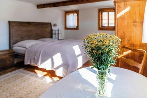 A bedroom with a bed, a bedside table, a chair, a window, and a vase with flowers on a table.