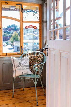 A room with a wooden floor, a metal chair with a floral cushion, a window with a stained glass design, and a door with a white frame.