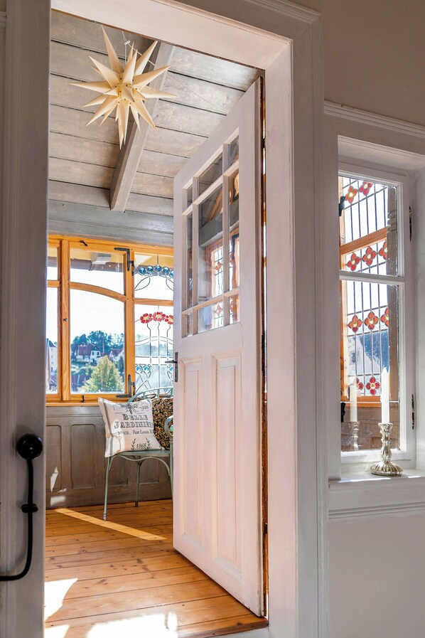 An open door leading to a room with a wooden floor, a bench, and a window with a view of the outside.