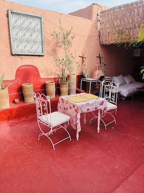 A red-walled room with a white metal table and chairs, a bench, and potted plants. - hannah house marrakech (Marrakech)