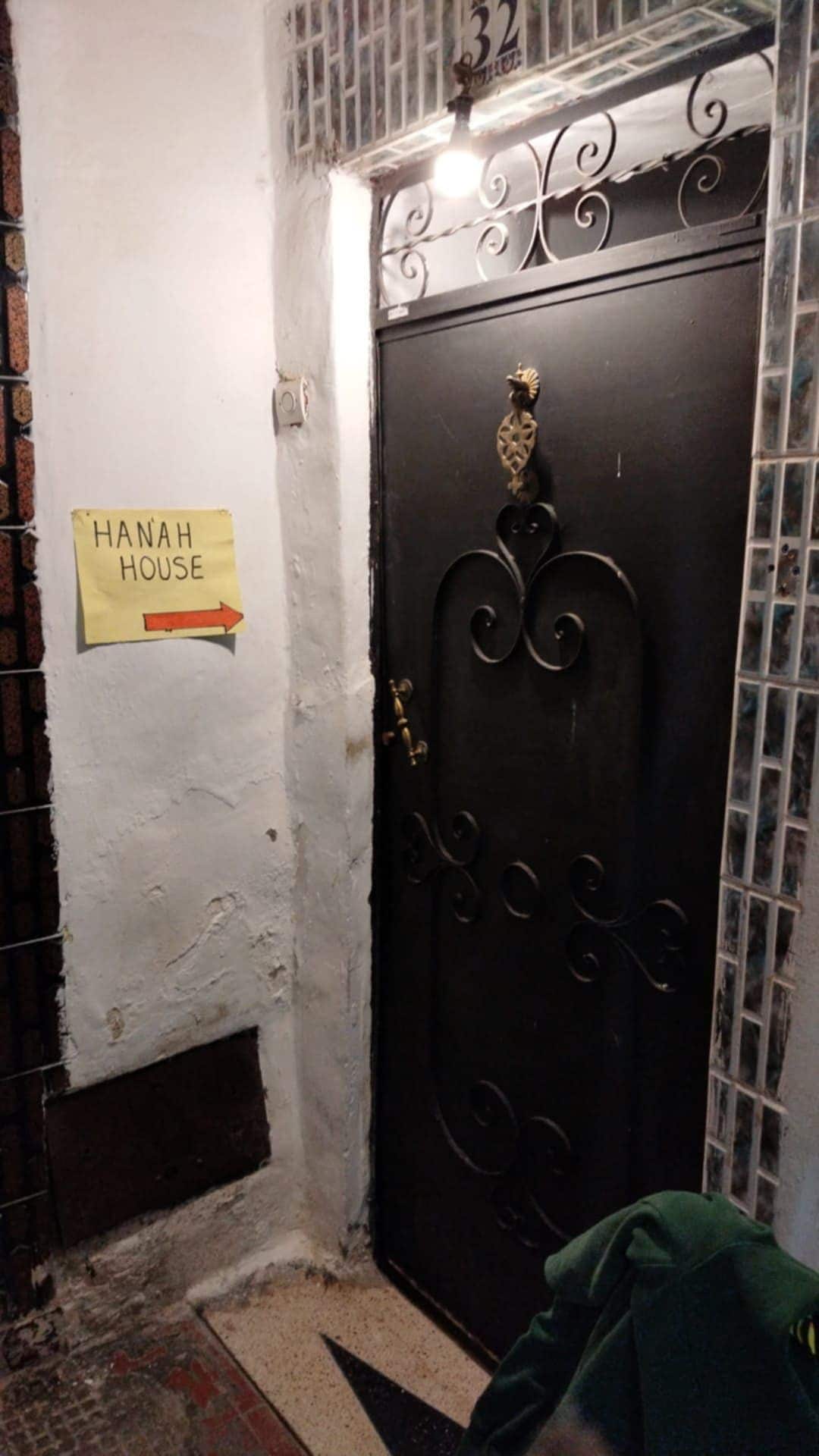 Una puerta negra con un tirador decorativo y un cartel que indica 'HANAH HOUSE' con una flecha señalando a la derecha.