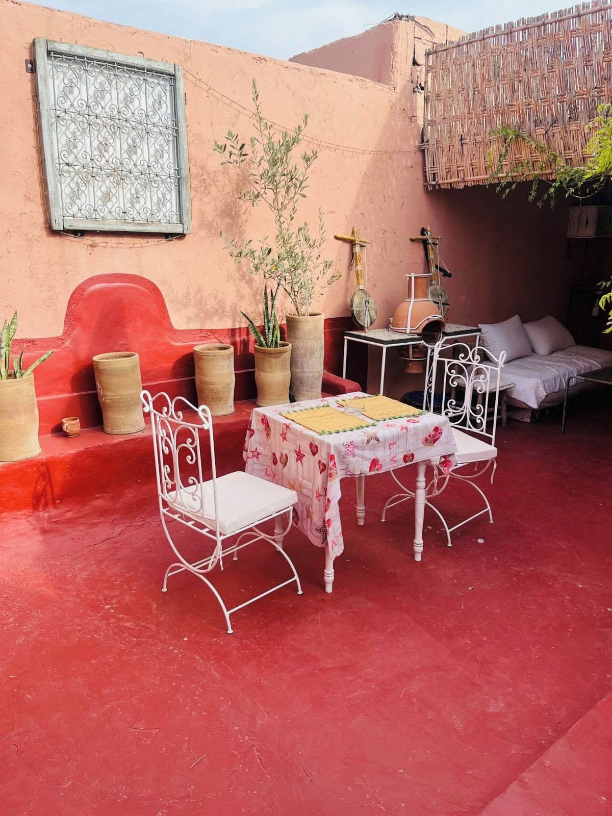 Un área de estar al aire libre con una mesa, sillas, plantas en macetas y una pared roja.