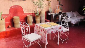 Un área de estar al aire libre con una mesa, sillas, plantas en macetas y una pared roja.