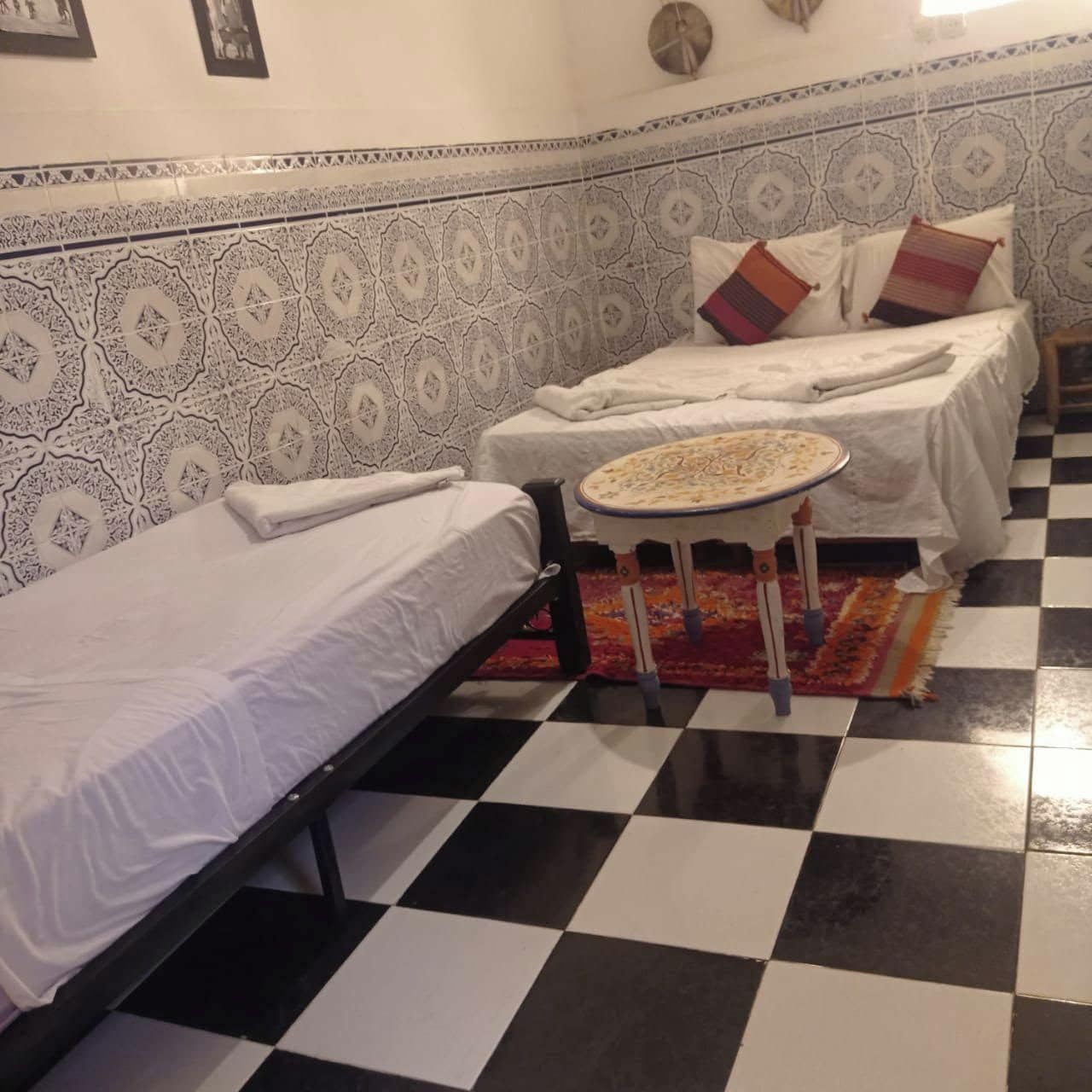 Una habitación con dos camas, una mesita redonda y baldosas estampadas en las paredes.