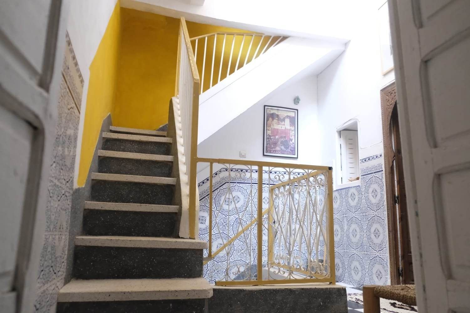Una escalera con una pared amarilla, barandilla blanca y un portón decorativo.
