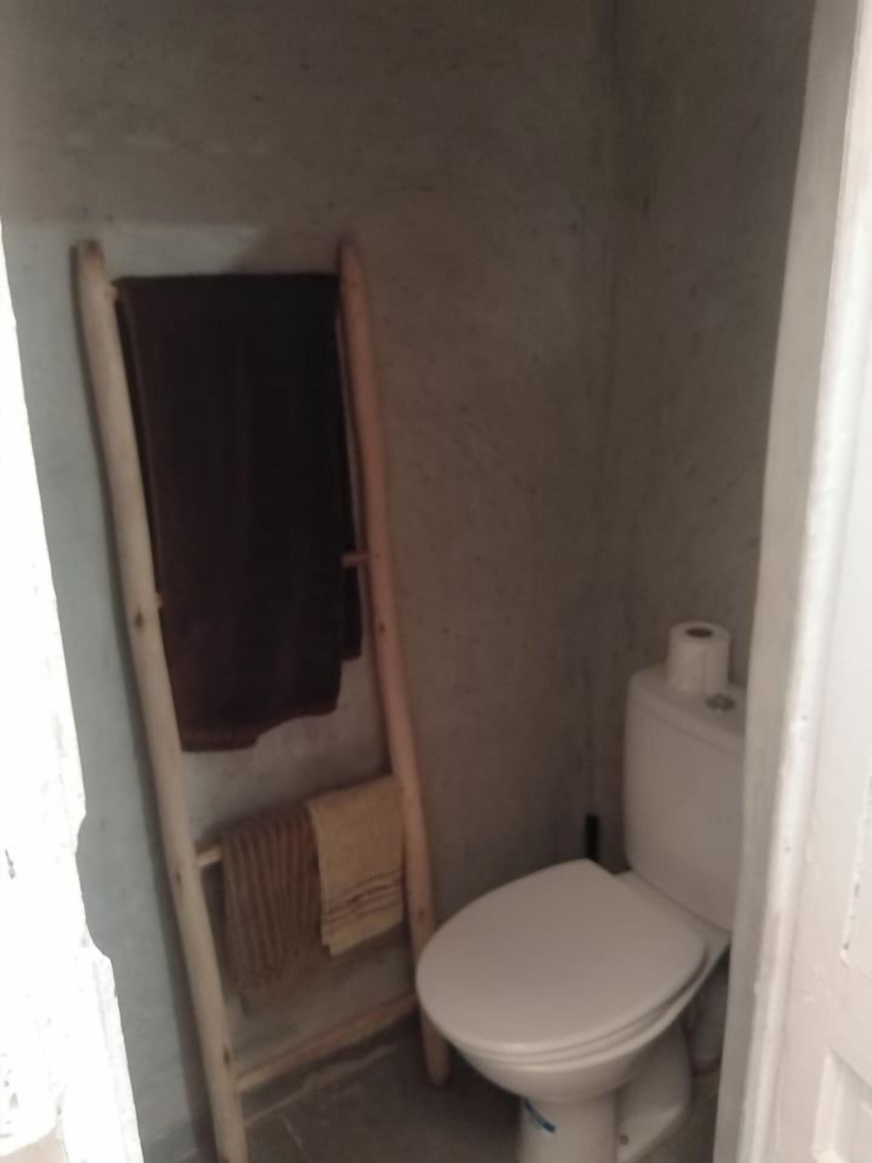 Un baño pequeño y estrecho con un inodoro, un perchero y un rollo de papel higiénico.