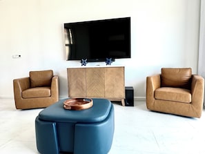 Un salon moderne avec deux fauteuils en cuir, un pouf bleu et un meuble en bois sur lequel est fixée une télévision à écran plat.
