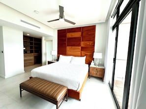 Een moderne hotelkamer met een groot bed, een houten hoofdbord, een bankje, nachtkastjes en een plafondventilator.