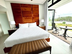 Een hotelkamer met een groot bed, een bankje, een nachtkastje met een lamp, een stoel en een tafel.