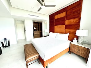 Une chambre d’hôtel moderne avec un grand lit, une tête de lit en bois, un banc, une table de chevet et une armoire.