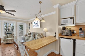 A kitchen with a wooden table, chairs, a microwave, and a coffee maker. - Tortuga Inn Beach Resort #219 | Direct Gulf & Beach Views (Bradenton Beach)
