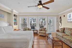 A bedroom with a bed, a ceiling fan, a window, and a door. - Tortuga Inn Beach Resort #219 | Direct Gulf & Beach Views (Bradenton Beach)