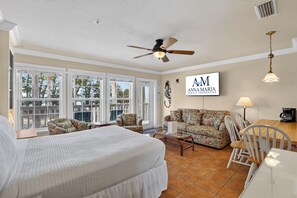 A bedroom with a bed, a sofa, a chair, a dining table, and a ceiling fan. - Tortuga Inn Beach Resort #219 | Direct Gulf & Beach Views (Bradenton Beach)