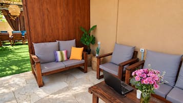 Un sofá de madera con cojines, un portátil sobre una mesa y un jarrón con flores.