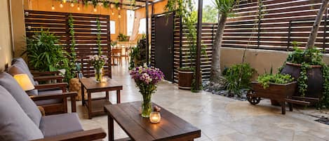 Un patio al aire libre con mobiliario de madera, una mesa con un jarrón de flores y una variedad de plantas en macetas.