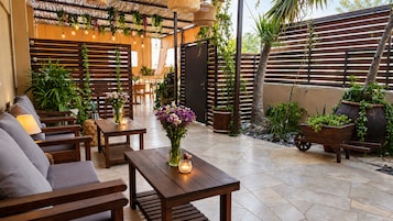 Un patio al aire libre con mobiliario de madera, una mesa con un jarrón de flores y una variedad de plantas en macetas.