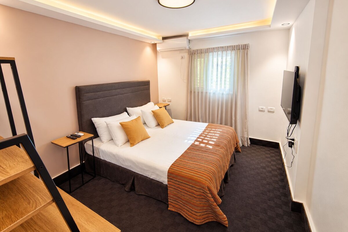 Habitación de hotel con cama, televisión, escritorio y ventana con cortinas.