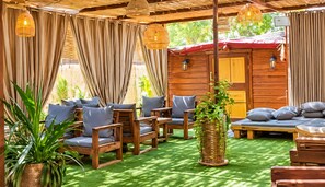 Un área de estar al aire libre con muebles de madera, una maceta tejida y luces colgantes.