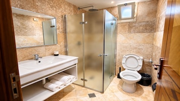 Un baño moderno con ducha envuelta en vidrio, un lavabo blanco con un espejo encima y un inodoro con un cubo de basura negro a su lado.